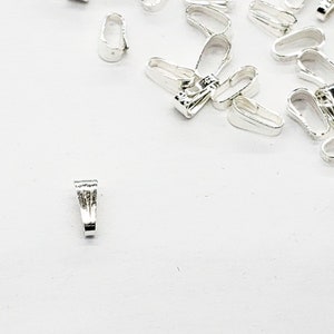 May include: A close-up of a pile of silver-toned metal jump rings. The jump rings are small and have a smooth, polished finish.