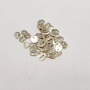 May include: A large pile of gold-colored metal jump rings. The rings are oval shaped and have a small keyhole design.