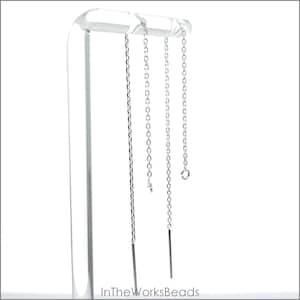 May include: Silver chain threader earrings displayed on a clear acrylic stand. The earrings have a delicate chain design with a straight bar at the bottom. The earrings are shown against a white background.