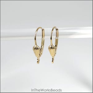 May include: A pair of gold-toned earring hooks with a decorative shell design. The hooks are made of metal and have a smooth finish.