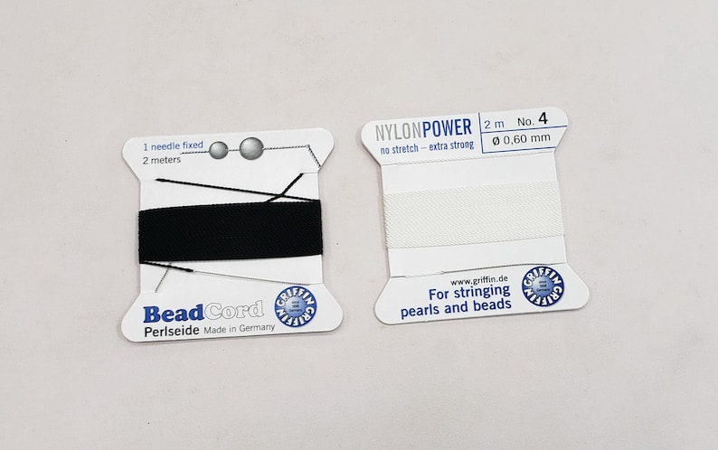 May include: Two spools of beading thread. The spool on the left is black and says "Bead Cord Periseide Made in Germany". The spool on the right is white and says "NYLONPOWER 2 m No. 4 0,60 mm no stretch - extra strong www.griffin.de For stringing pearls and beads".
