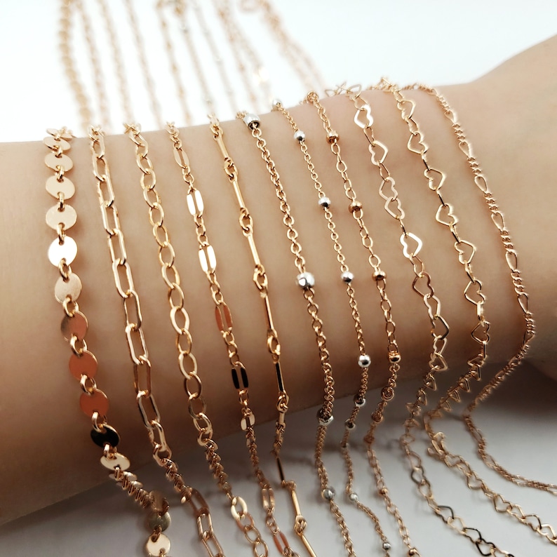 May include: A collection of gold chain bracelets with different styles, including a coin chain, a cable chain, a curb chain, a box chain, a heart chain, and a beaded chain.