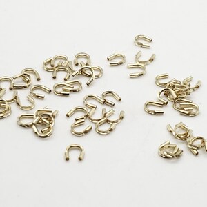 Op de afbeelding: Een grote hoeveelheid gouden metalen springringen. De ringen zijn klein en hebben een U-vorm.