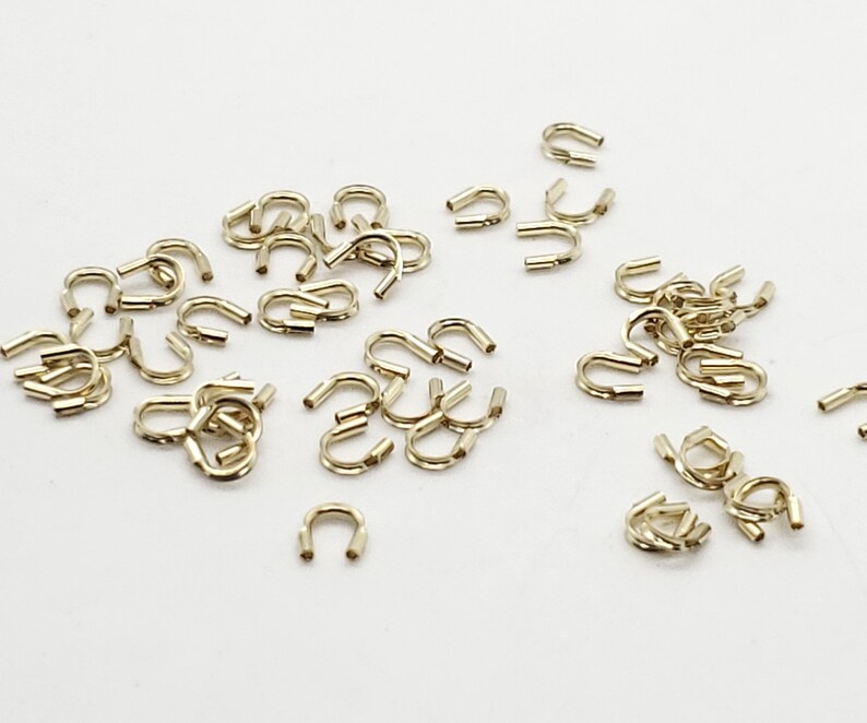 Op de afbeelding: Een grote hoeveelheid gouden metalen springringen. De ringen zijn klein en hebben een U-vorm.