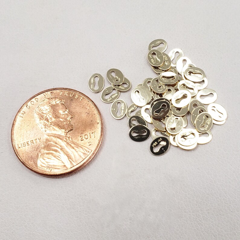 May include: A pile of gold-colored metal jump rings, each with a small keyhole-shaped opening. The jump rings are about the size of a US penny.