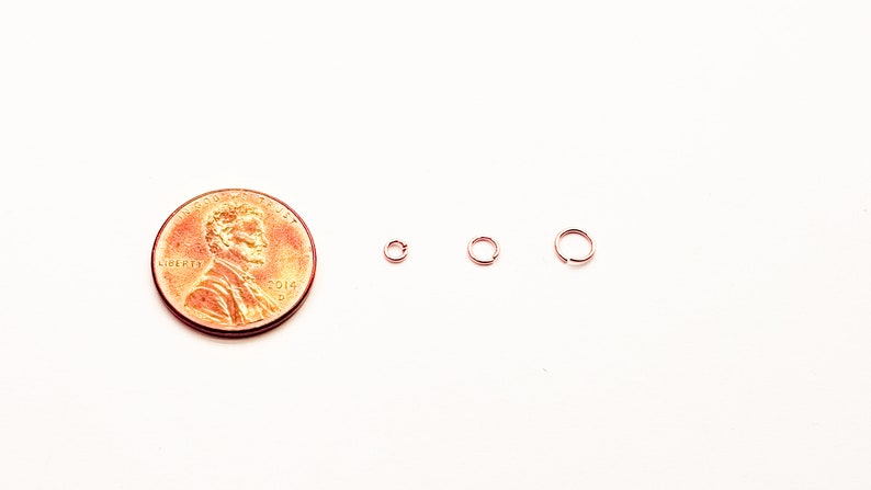 May include: Three small gold jump rings, each with a different diameter, are shown next to a US penny for size comparison.