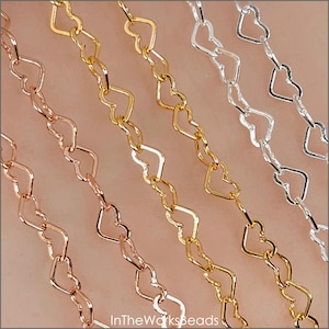 May include: Close-up of four chains in rose gold, gold, and silver. Each chain is made of heart-shaped links. The chains are displayed diagonally against a neutral background. The text "InTheWorksBeads" is visible in the bottom left corner.
