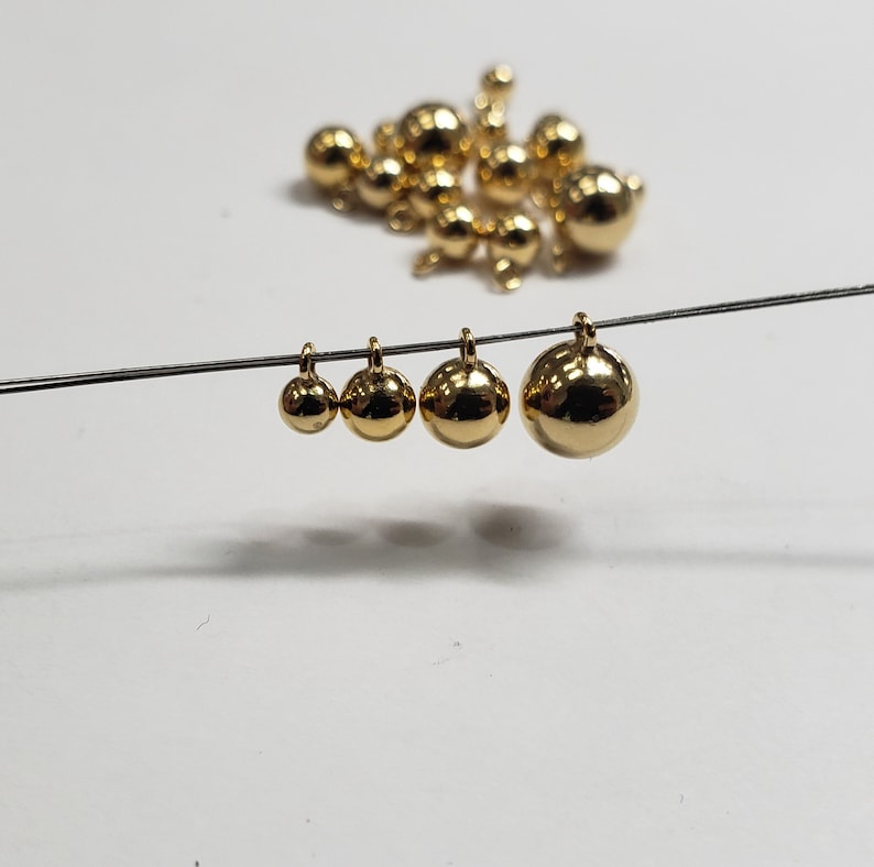 May include: Four gold-colored metal balls of different sizes hanging from a wire. The balls are smooth and round.