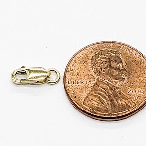Puede incluir: Cierre de metal dorado para un collar o pulsera, mostrado junto a un centavo de d&oacute;lar estadounidense para comparar el tama&ntilde;o.