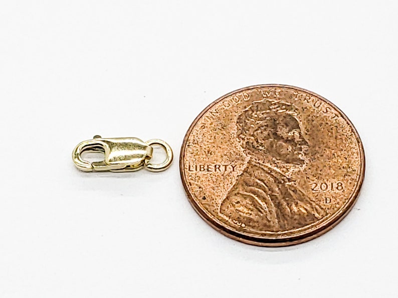 Puede incluir: Cierre de metal dorado para un collar o pulsera, mostrado junto a un centavo de d&oacute;lar estadounidense para comparar el tama&ntilde;o.