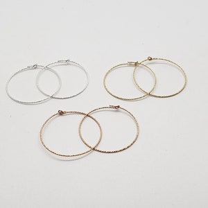 May include: Three pairs of hoop earrings in silver, gold, and rose gold. The earrings are all the same size and have a twisted wire design.