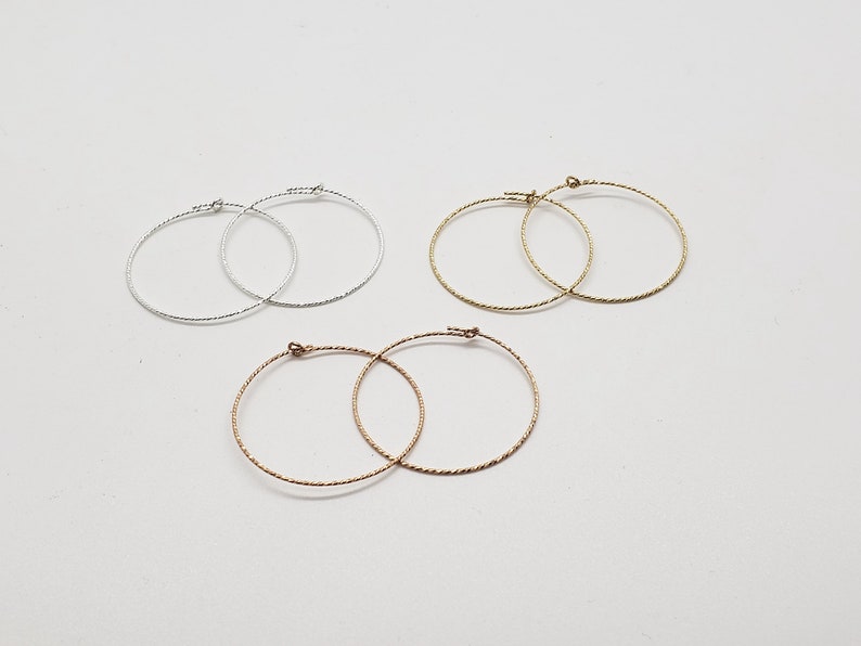 May include: Three pairs of hoop earrings in silver, gold, and rose gold. The earrings are all the same size and have a twisted wire design.