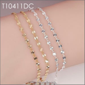 May include: Four delicate bracelets with a floral design. Two are gold-toned, and two are silver-toned. The bracelets are displayed on a person's arm. The text "T10411DC" is in the upper left corner.