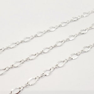 May include: Three strands of silver-coloured chain with an oval and figure-eight link design. The chains are arranged diagonally across a white background, creating a pattern of repeating shapes.