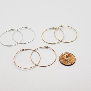May include: Three pairs of hoop earrings in silver, gold, and rose gold. The earrings are all the same size and have a twisted wire design. A penny is included for size reference.