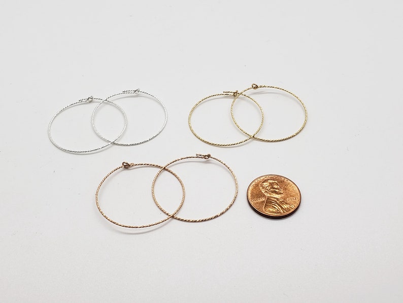 May include: Three pairs of hoop earrings in silver, gold, and rose gold. The earrings are all the same size and have a twisted wire design. A penny is included for size reference.