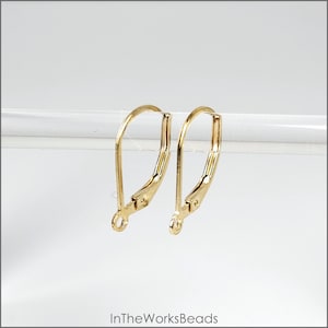 May include: Two gold-toned earring hooks, also known as French hooks, are shown against a white background. The hooks are made of metal and have a smooth finish.