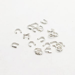 Op de afbeelding: Een groep zilverkleurige metalen springringen, ook wel springringen genoemd, liggen verspreid op een wit oppervlak. Deze ringen worden gebruikt om juweelcomponenten te verbinden.