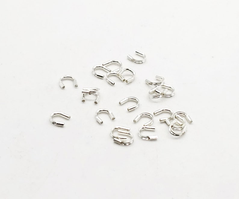 Op de afbeelding: Een groep zilverkleurige metalen springringen, ook wel springringen genoemd, liggen verspreid op een wit oppervlak. Deze ringen worden gebruikt om juweelcomponenten te verbinden.