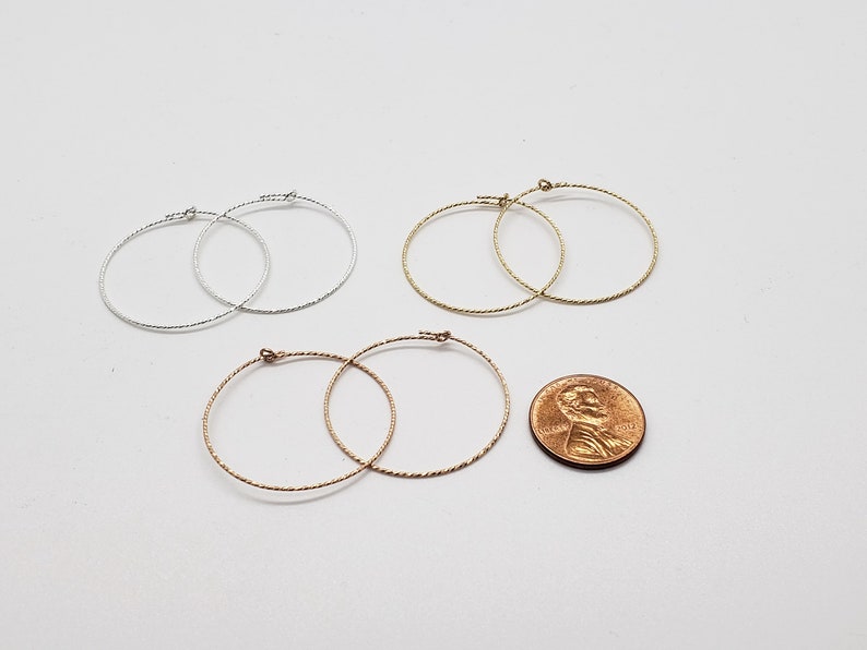May include: Three pairs of hoop earrings in silver, gold, and rose gold. The earrings are all the same size and have a textured, twisted design. A penny is included for size reference.