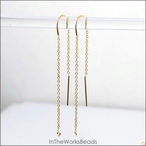 May include: A pair of gold dangle earrings with a chain and a small bar hanging from each earring.