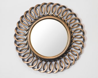 May include: A round mirror with a decorative, ornate frame made of interlocking circles. The frame is a dark bronze color with a gold finish.