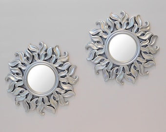 May include: Two silver-toned decorative mirrors with a sunburst design. Each mirror has a round, reflective surface surrounded by a frame of stylized leaves.