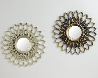 May include: Two decorative wall mirrors. One mirror has a silver finish with a petal-like design around a circular mirror. The other mirror has a gold and black finish with a similar petal design around a circular mirror.