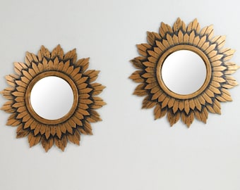 May include: Two gold sunburst mirrors with a black outline and a round mirror in the center.