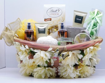 May include: A decorative gift basket filled with various items, including a box of Lindt Lindor white chocolate, vanilla-scented products, a candle, and a loofah. The basket is adorned with white and yellow flowers and a butterfly.