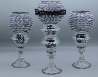 May include: Three decorative candle holders. Each has a clear glass base and stem, topped with a silver beaded orb. The center holder has a black beaded accent. The bases and stems are adorned with rhinestones.