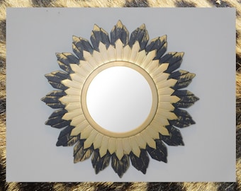 May include: A gold and black sunburst mirror with a round reflective surface. The mirror has a distressed finish and a decorative design.