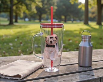 May include: A clear double-walled tumbler with a red lid and straw, featuring a graphic of a puppy wearing glasses and a bow tie. A stainless steel water bottle sits next to the tumbler on a wooden surface. A beige cloth is also on the wooden surface.