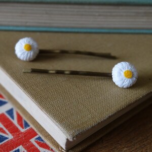 May include: Two gold hair clips with white daisy flower accents. The daisies have yellow centers.