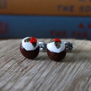 May include: A pair of silver stud earrings with a miniature Christmas pudding design. The pudding is brown with white icing and a red holly berry on top.