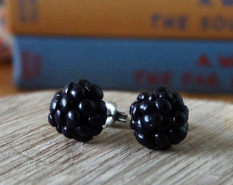 May include: A pair of black stud earrings shaped like blackberries. The earrings are on a wooden surface.