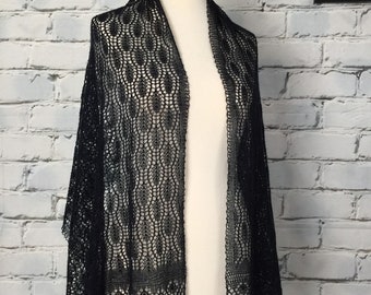 May include: A black lace shawl with a delicate pattern, draped over a white mannequin. The shawl is made of a fine, lightweight fabric and has a scalloped edge.