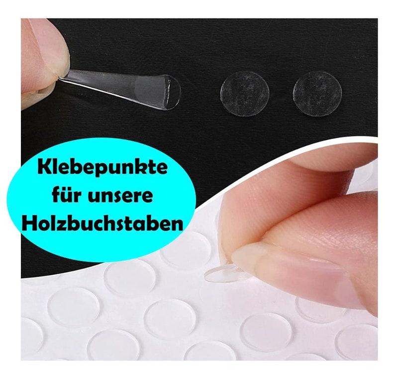 May include: A sheet of clear adhesive dots, also known as sticky dots, for use with wooden letters. The image shows a hand peeling off a dot from the sheet. The text on the sheet reads "Klebepunkte f&uuml;r unsere Holzbuchstaben".