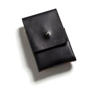 May include: Black leather card holder with a silver button closure and the word "FRIGGA" embossed on the front.