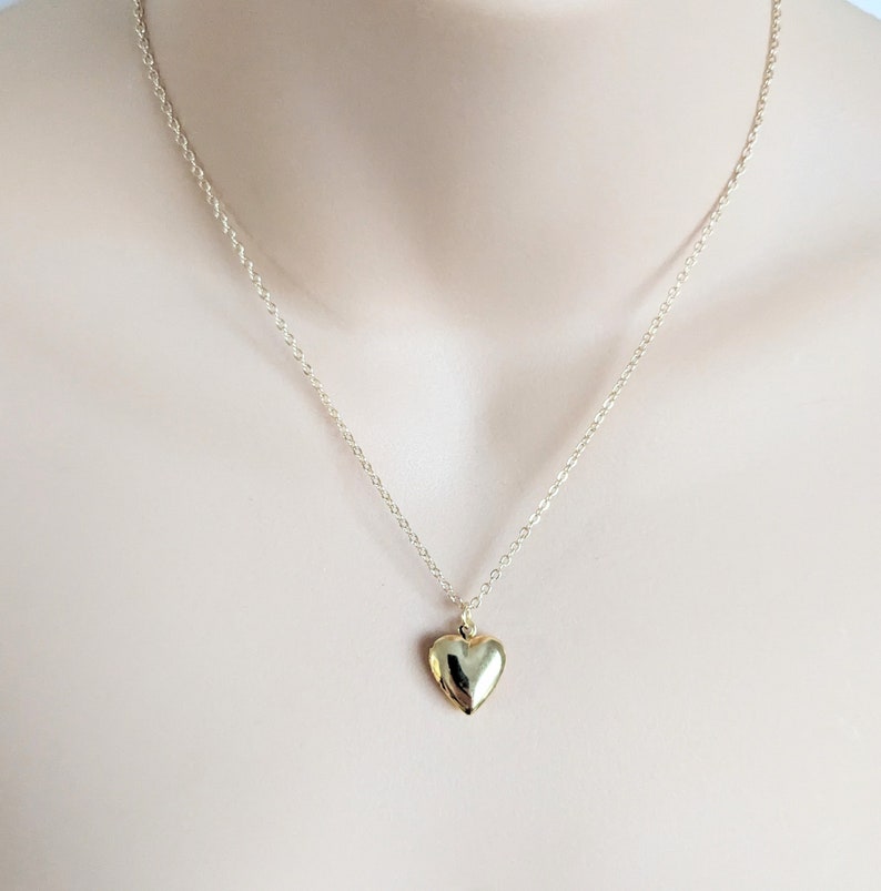 Puede incluir: Un collar con colgante de coraz&oacute;n dorado. El dije en forma de coraz&oacute;n cuelga de una delicada cadena. El collar se muestra sobre un fondo neutro, resaltando el dise&ntilde;o de la joya.