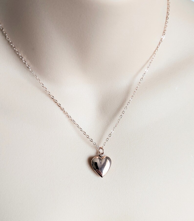 Puede incluir: Un delicado collar con un peque&ntilde;o colgante de coraz&oacute;n pulido. El coraz&oacute;n es de color plateado brillante y cuelga de una fina cadena. El collar se muestra sobre un fondo neutro, destacando la sencilla elegancia de la joya.