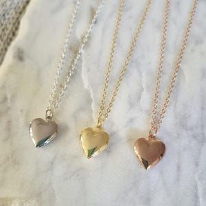 Puede incluir: Tres collares con colgantes en forma de coraz&oacute;n, plata, oro y oro rosa. Cada collar tiene una cadena delicada y un medall&oacute;n pulido en forma de coraz&oacute;n. Los colgantes se muestran sobre una superficie de m&aacute;rmol blanco.