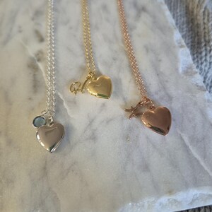 Puede incluir: Tres collares con colgantes en forma de coraz&oacute;n en plata, oro y oro rosa. El collar de plata tiene un dije de piedra preciosa azul. El collar de oro tiene un dije inicial. El collar de oro rosa tiene un dije de estrella.