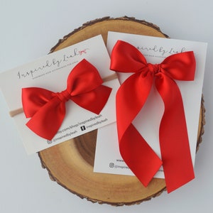 May include: Two red satin hair bows, one on a headband and one with long tails. The bows are handmade and are available for purchase on Etsy.