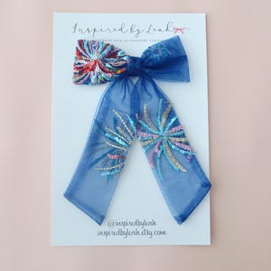 Könnte beinhalten: Eine blaue Haarschleife mit einem paillettenbesetzten Mittelteil und kaskadierenden Bändern. Die Schleife hat ein Paillettendesign in Rot, Blau und Gold. Die Schleife ist an einer weißen Karte mit dem Text "Inspired by Leah" und der Etsy-Shop-URL befestigt.