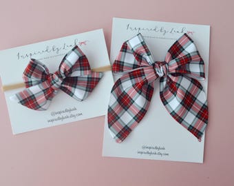 May include: Two plaid hair bows, one small and one large, in red, white, and green plaid. The bows are on white cards with the text "Inspired by Leah" and social media information.