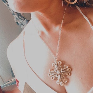 May include: A silver necklace with a large, intricate snowflake pendant. The pendant is made of many small, delicate pieces of metal that are joined together to create a complex design.