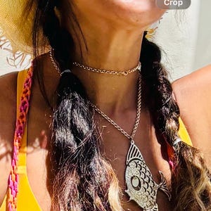May include: Gold-toned necklace featuring a fish pendant with a rhinestone design. The necklace has a delicate chain and a matching choker. The image shows a close-up of the necklace against a yellow background.