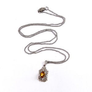 May include: A silver chain necklace with a pendant featuring a brown gemstone set in a silver filigree design.