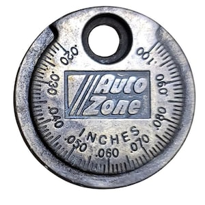 May include: A silver spark plug gap gauge with the "Auto Zone" logo. The gauge has a circular design with measurements in inches, ranging from .020 to .100. It features a hole at the top for hanging.